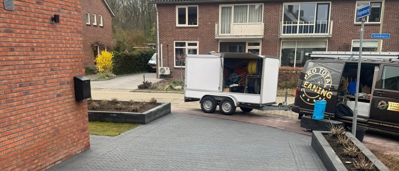 De bedrijfsbus met hogedrukaanhanger op een pas gereinigde oprit