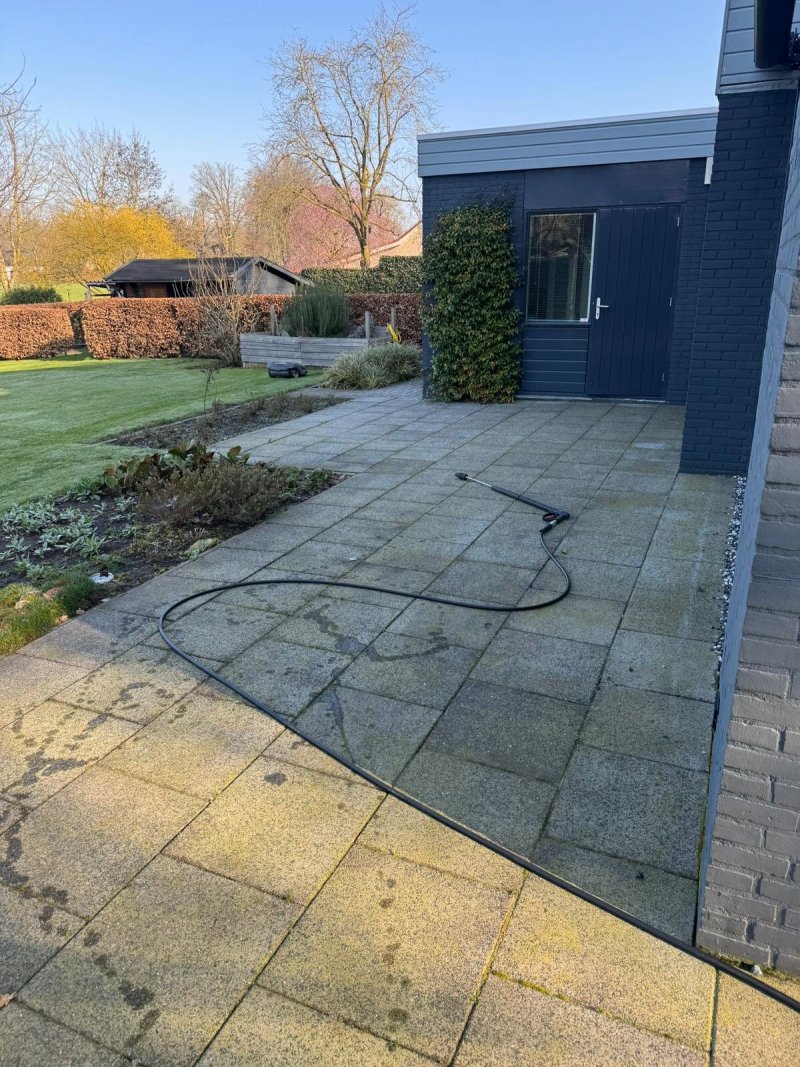 Ruim tegelterras met gele en groene aanslag, met de slang er nog overheen